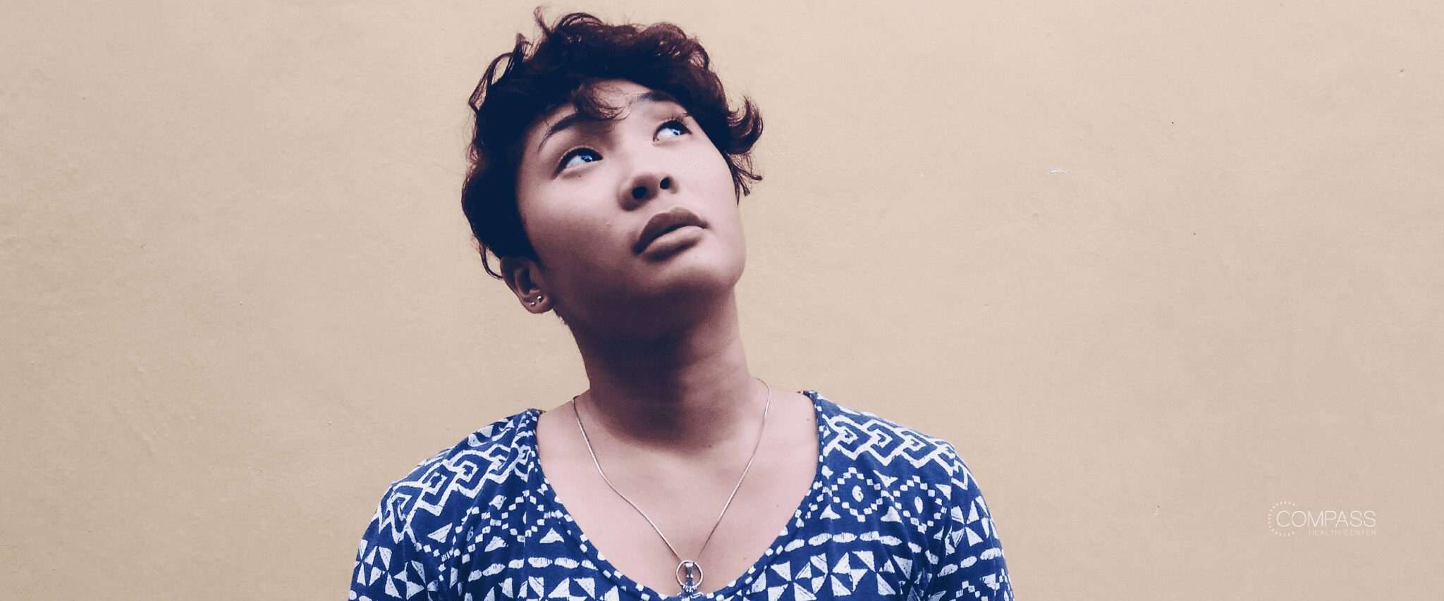 A woman standing against a neutral wall looking upwards