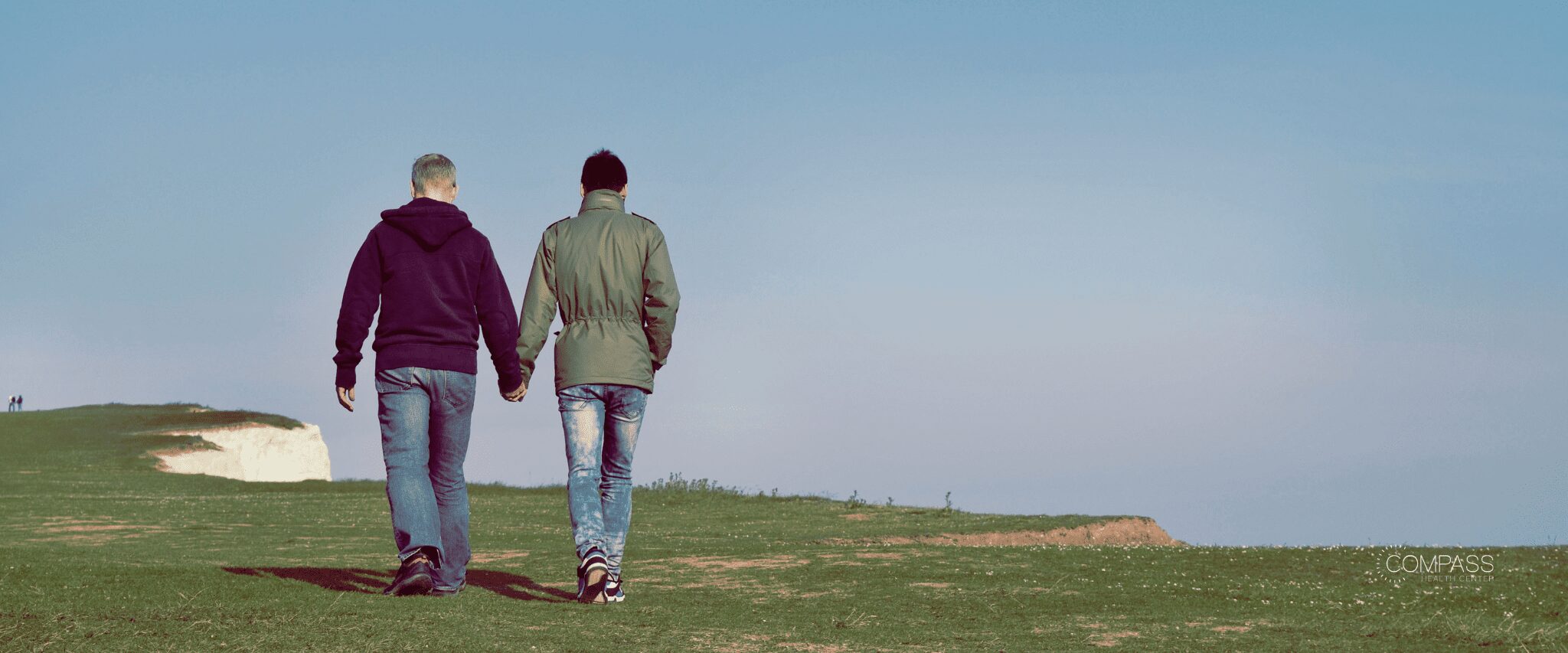 A couple holding hands and walking along a cliff covered in green grass Image source: Unsplash