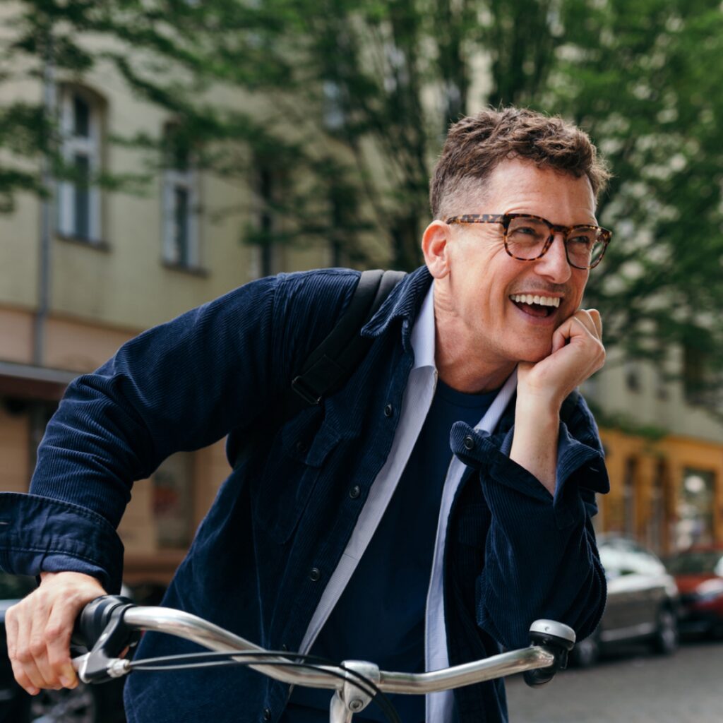man smiling on a city street, riding a city bike.