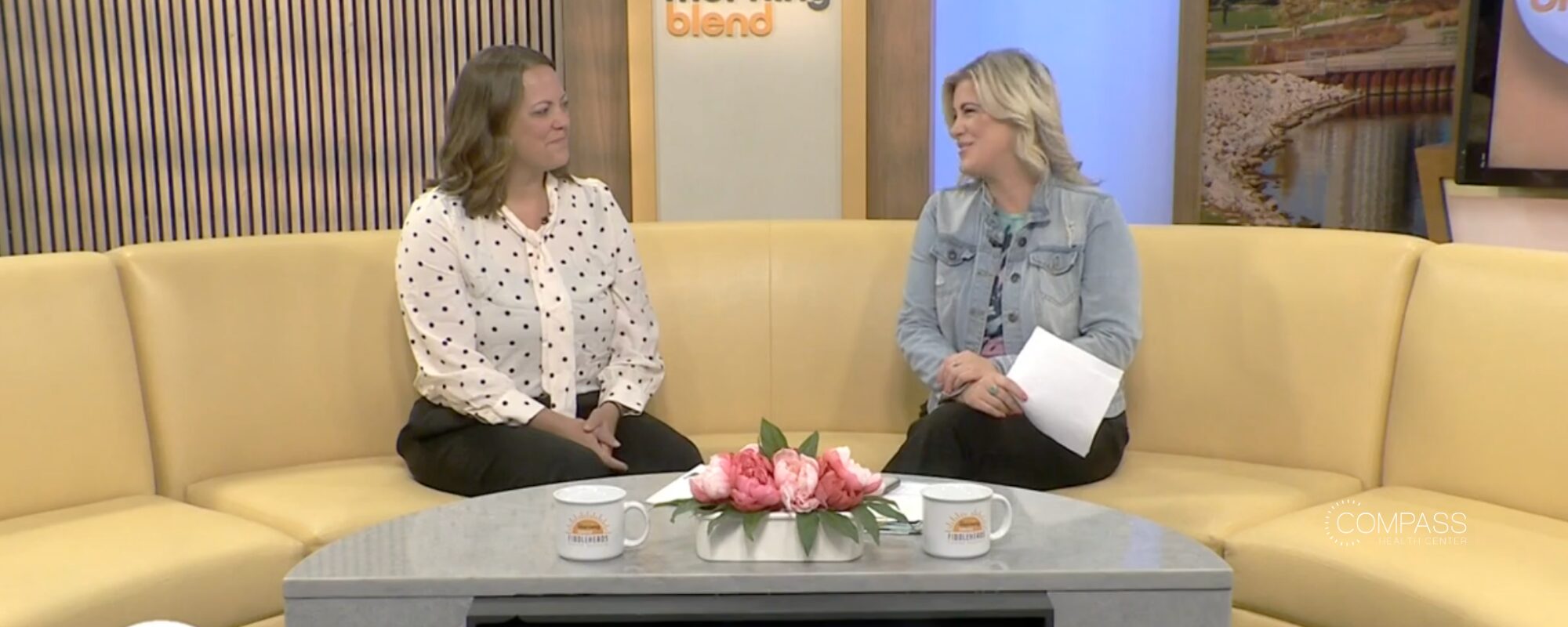 Two women on the set of The Morning Blend sit on a yellow semicircle couch, absorbed in conversation.
