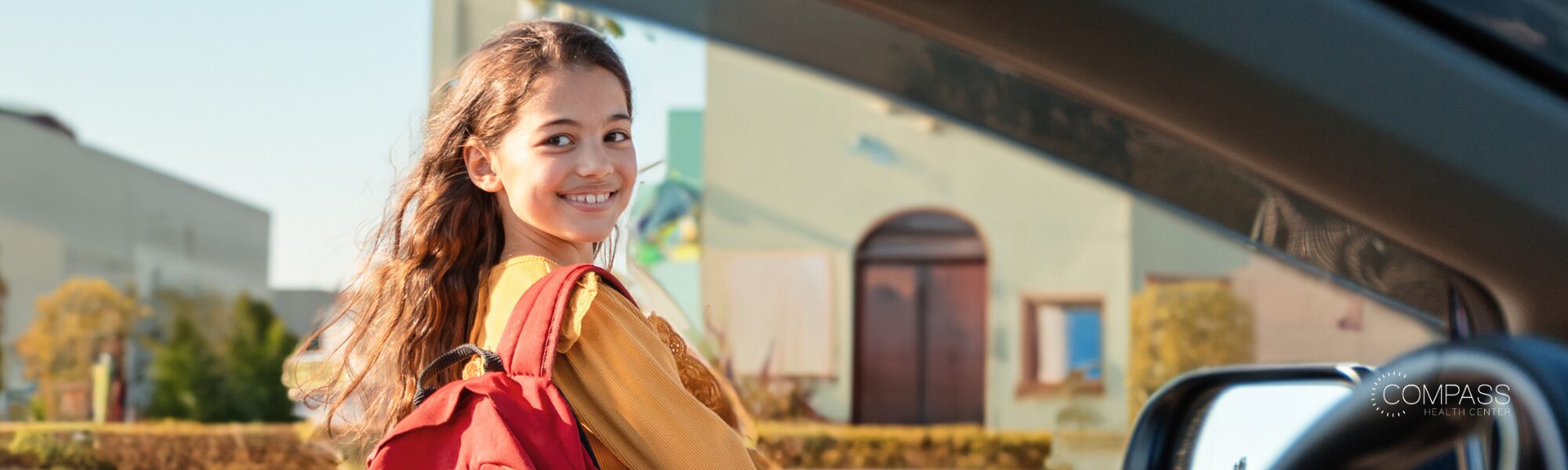 A young girl smiles while getting into a car outside her school.