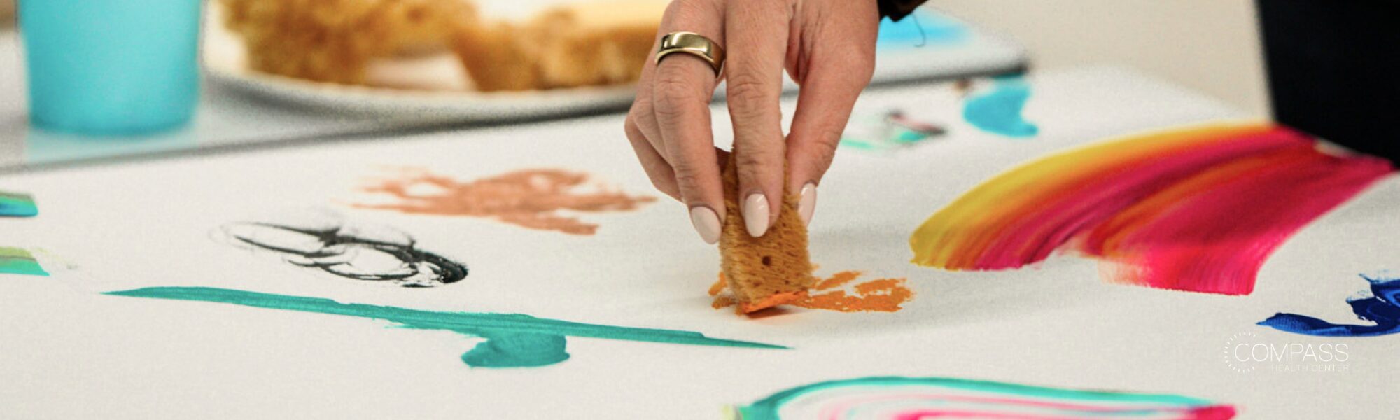 A hand uses a sponge to create colorful artwork with paint.